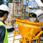 Worker standing in front of the concrete mixer, holding smart phone